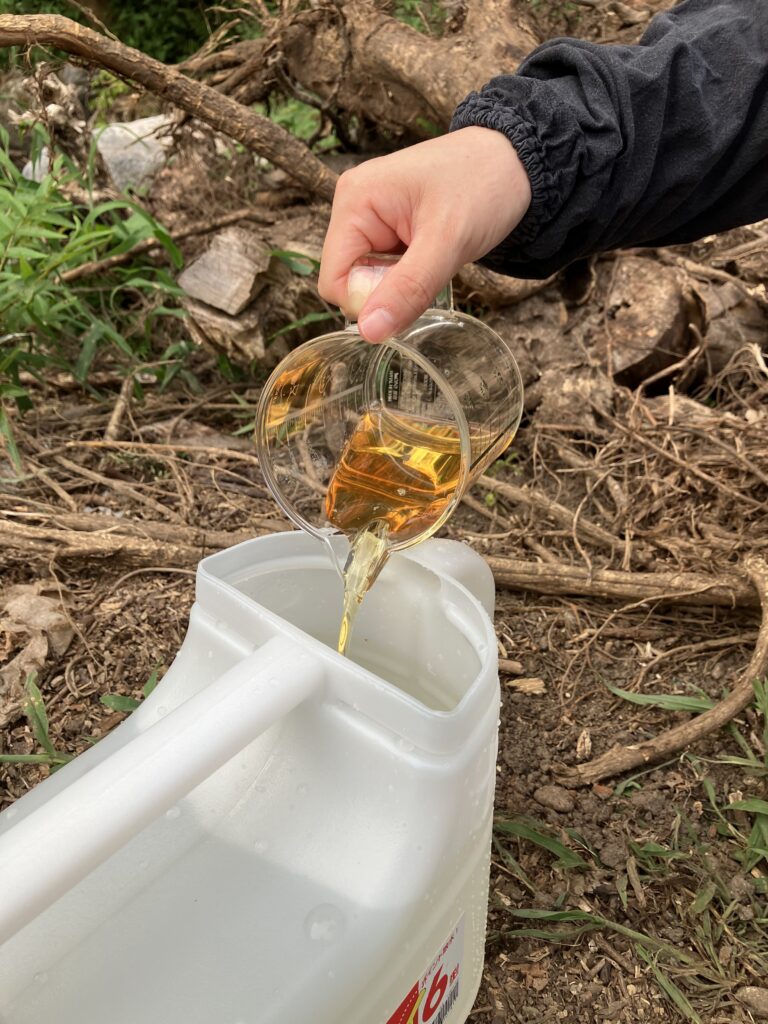 計量カップで測ったサンフーロンを、散布用の水が入ったジョウロに注いで50倍希釈の除草液を作る様子