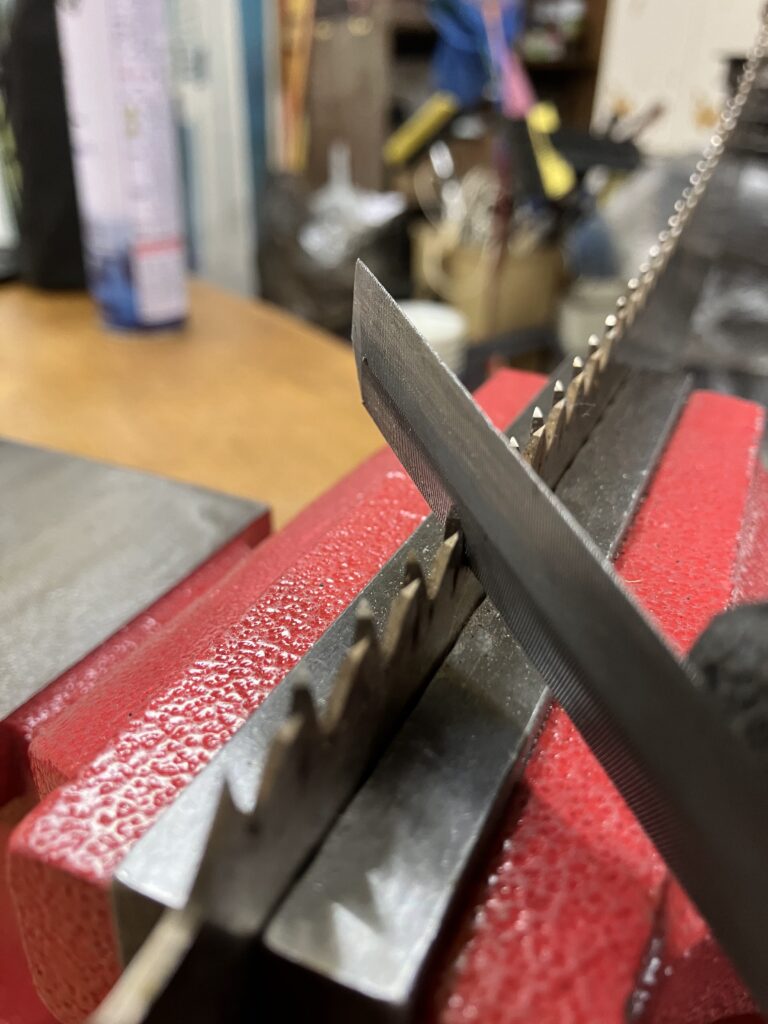 ノコギリの刃に両刃ヤスリを当てて研いでいる様子。目立ての実践シーン。