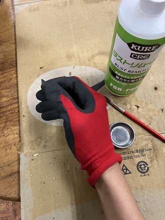 レバーホイストの錆び取り作業で、酸性のラストリムーバーを扱う前に手袋を着用している写真。