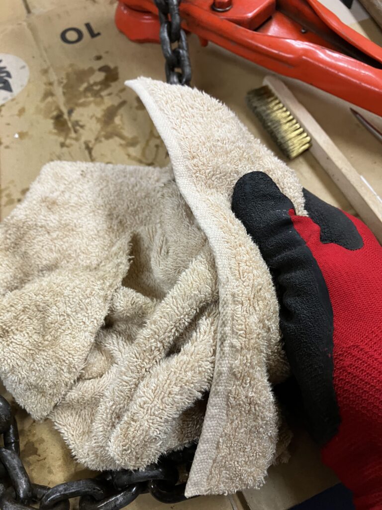 レバーホイストのチェーンをウエスとパーツクリーナーで汚れを落としている様子。