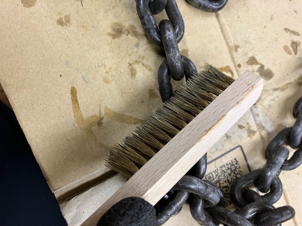 ラストリムーバーで浮いた錆を真鍮ブラシで丁寧に落としているレバーホイストのチェーンの写真。