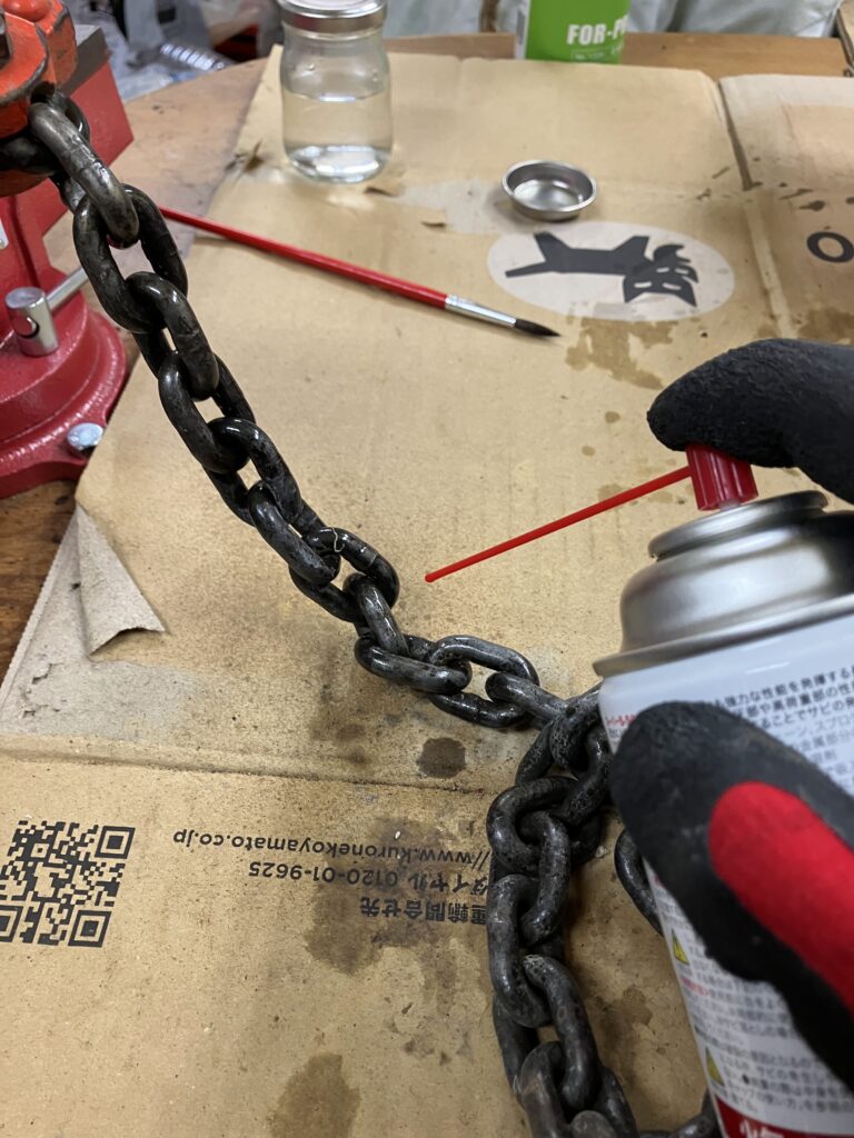 錆び取り後のレバーホイストのチェーンにKURE 5-56を吹きかけて防錆処理をしている写真。