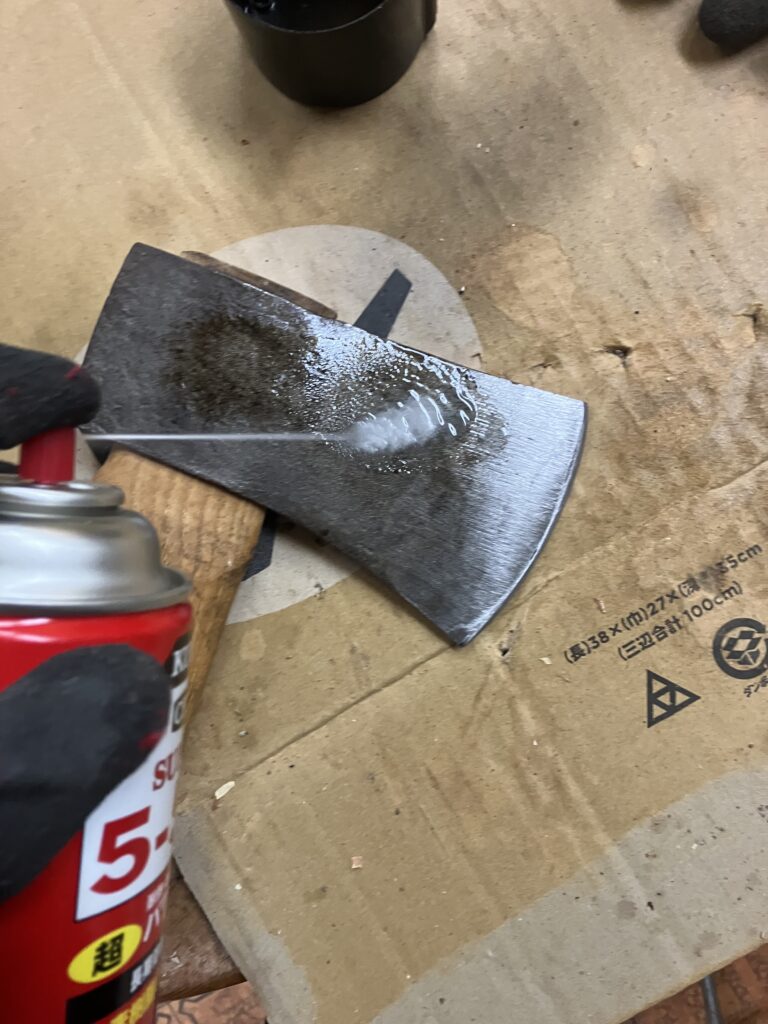 刃こぼれ修理を終えた斧に錆止めスプレーをかけて仕上げている様子。