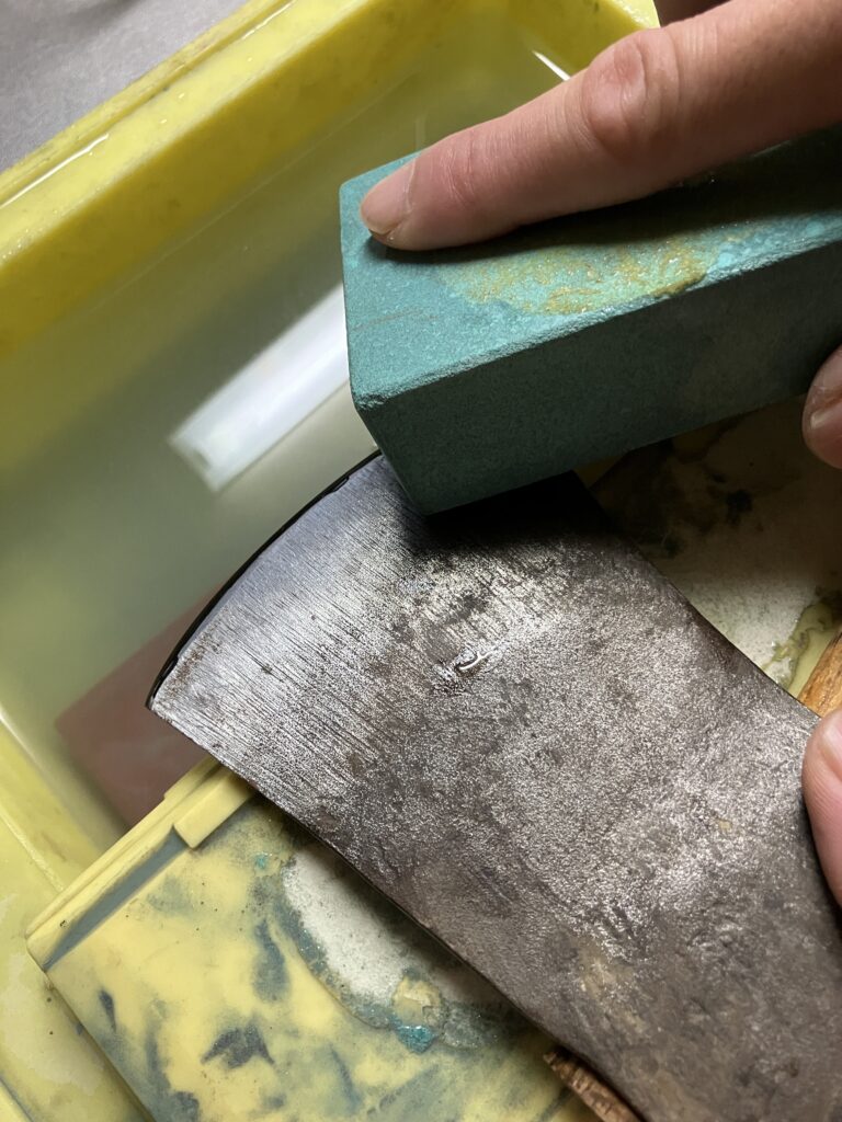 砥石を使って斧の刃を研いでいる様子。