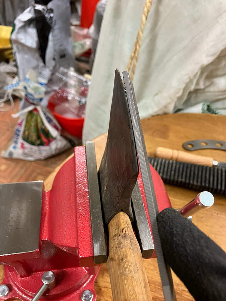 鉄工ヤスリの荒目で刃こぼれした斧の刃先を削って修理している写真