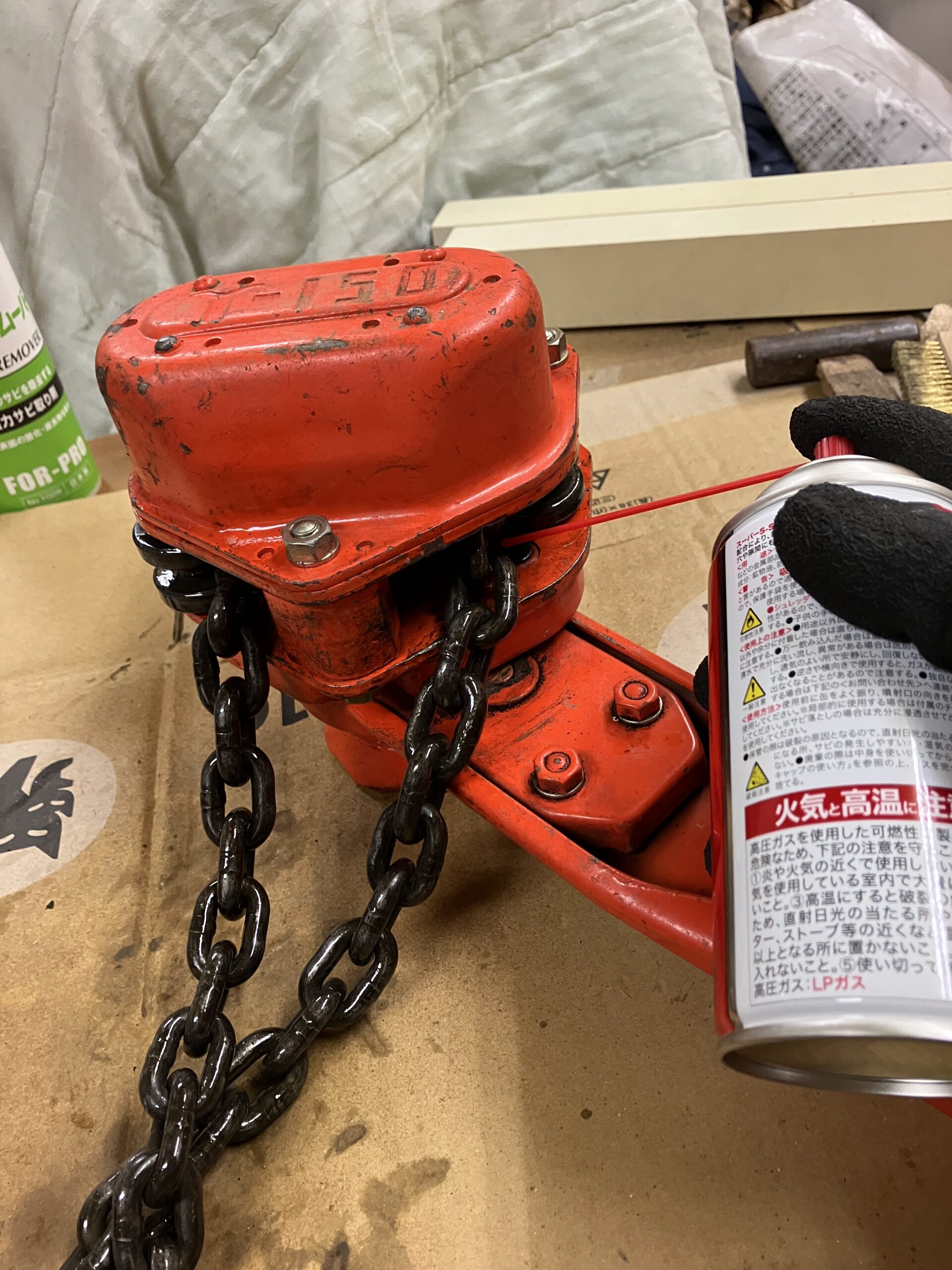 レバーホイストのチェーンにサビ取り剤を吹きかけて清掃している作業